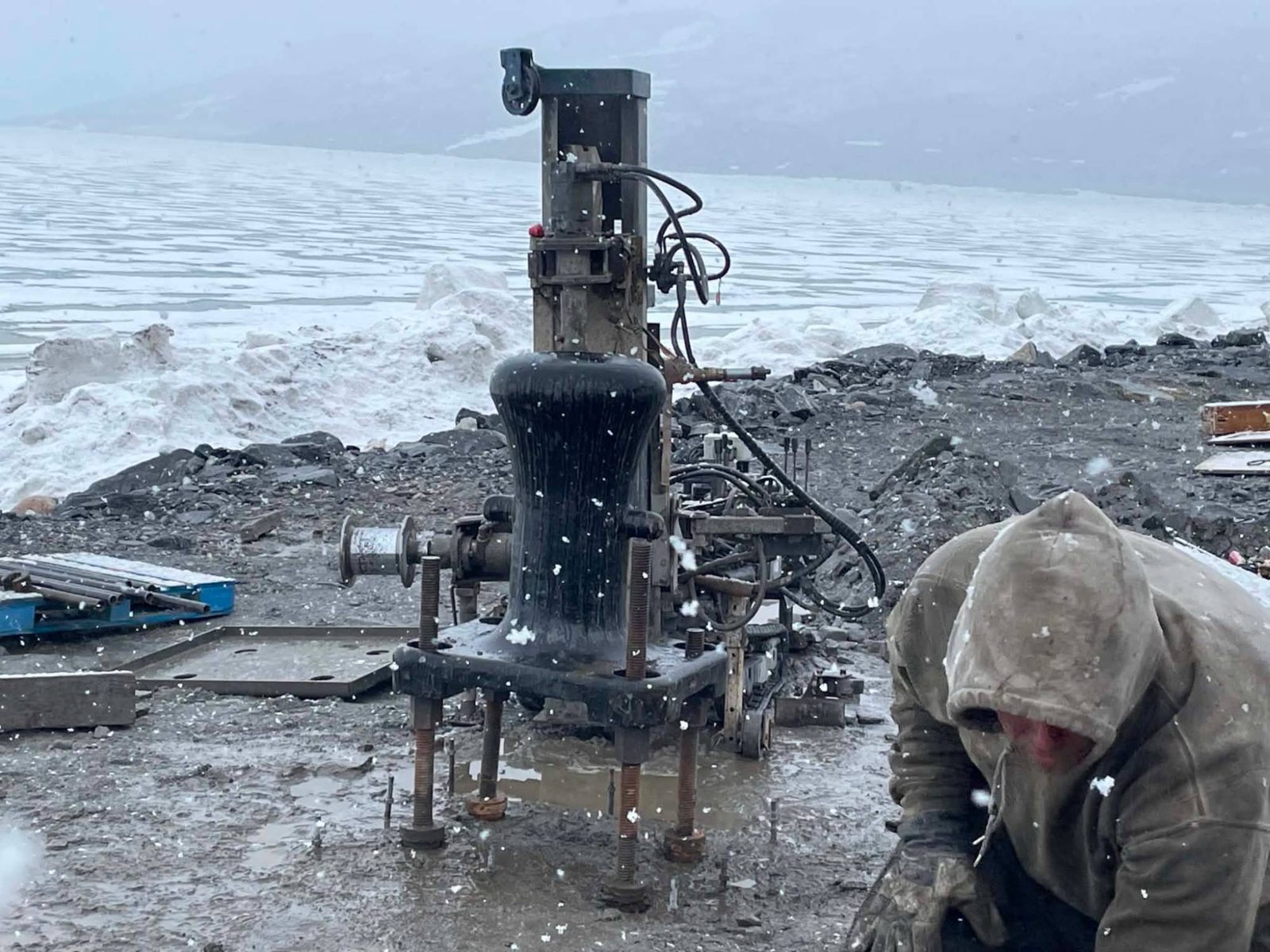 Foreur au travail sous la neige, à côté d'une foreuse compacte, au bord d'une mer glacée
